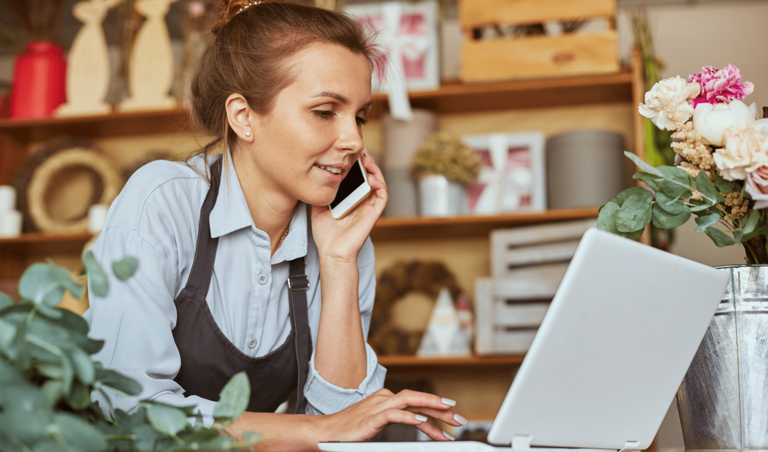 Florist handling phone and online orders using laptop in flower shop workspace