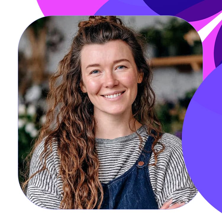 portrait of young female florist smiling in shop facing camera with iris, fuchsia and violet motif.