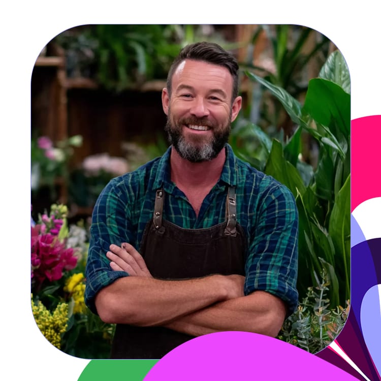 portrait of male florist smiling in shop facing camera with multi-color motif.