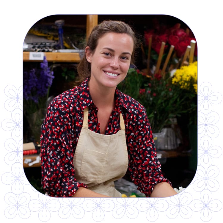 portrait of young female florist smiling in shop facing camera with motif pattern background
